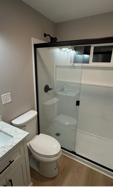 Bathroom with a sliding glass shower door, white surround, toilet and white vanity