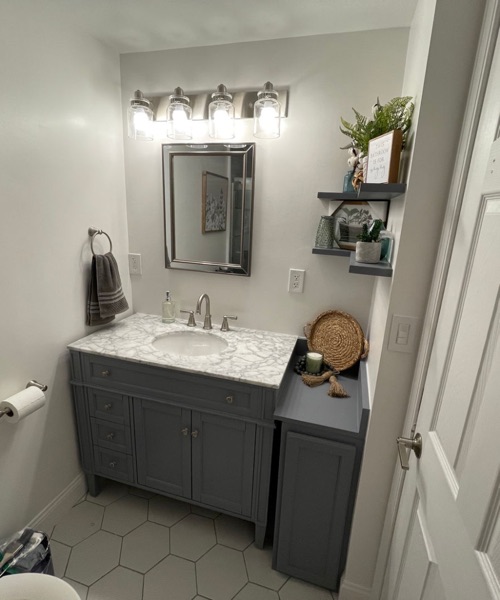 Bathroom with a gray vanity, marble-look top, framed mirror and four-light fixture
